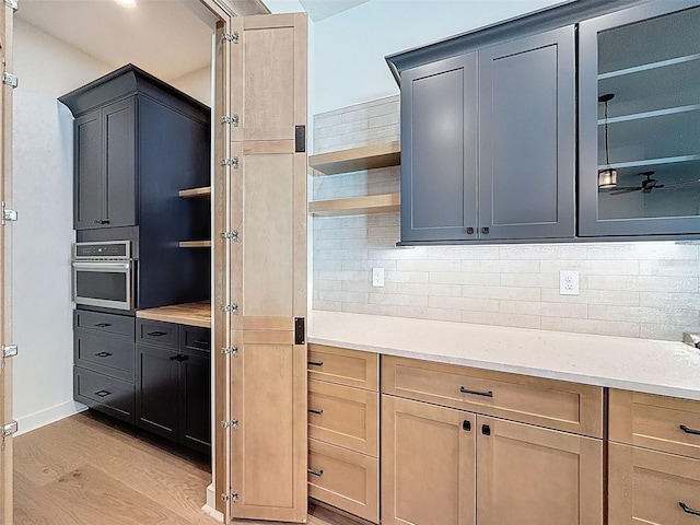 kitchen featuring open shelves, stainless steel oven, light wood-style flooring, and tasteful backsplash