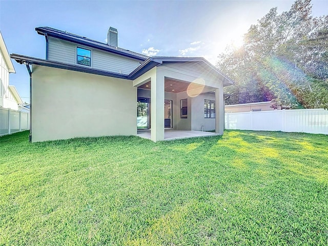 rear view of house with a lawn, stucco siding, a chimney, and a patio area