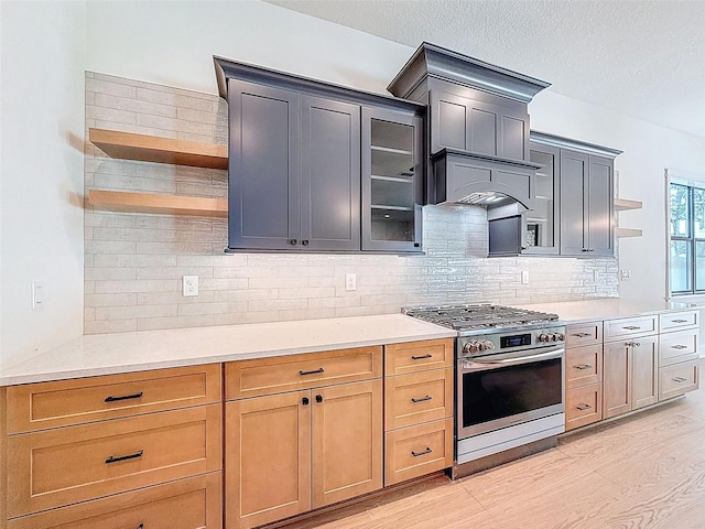 kitchen with open shelves, stainless steel range with gas stovetop, light wood-type flooring, backsplash, and glass insert cabinets