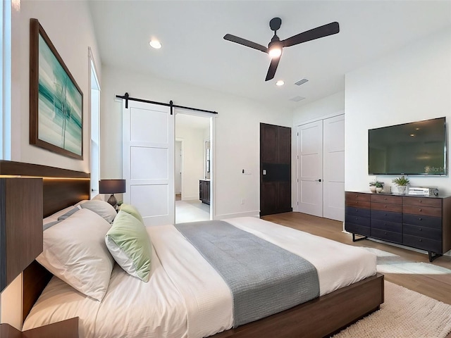 bedroom featuring light wood-style floors, a barn door, ensuite bathroom, and visible vents