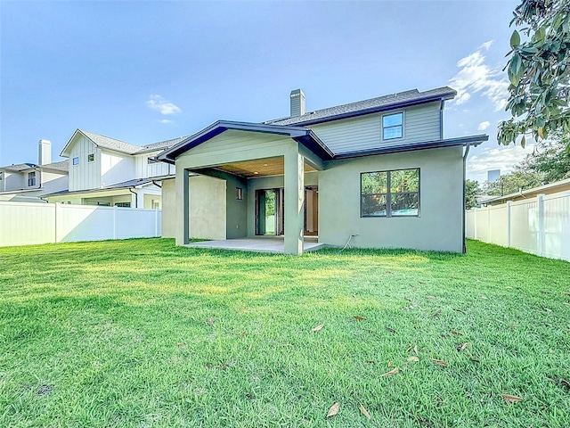 rear view of property featuring a chimney, a lawn, fence, a patio, and stucco siding