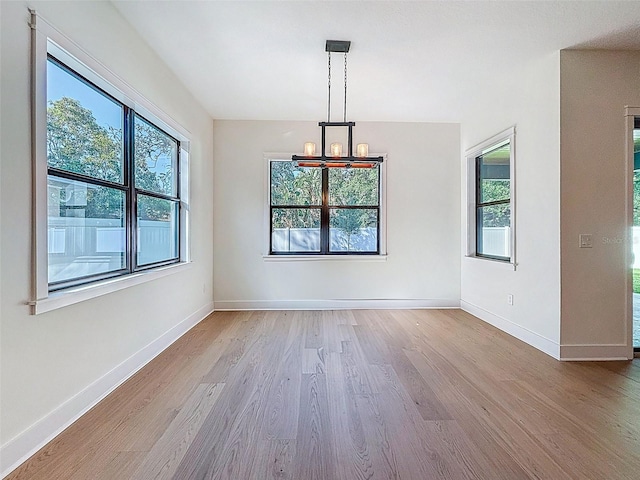 unfurnished dining area with wood finished floors, a notable chandelier, and a wealth of natural light
