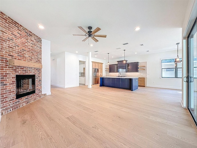 unfurnished living room featuring ceiling fan, a sink, light wood-style floors, a brick fireplace, and baseboards