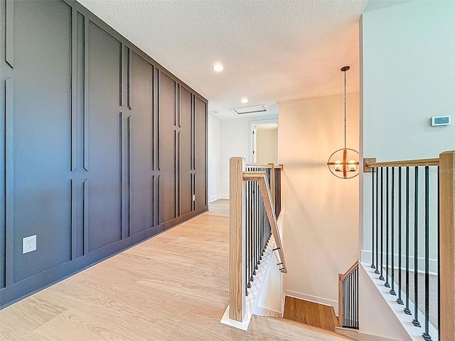 corridor with a textured ceiling, baseboards, an upstairs landing, recessed lighting, and light wood-style flooring