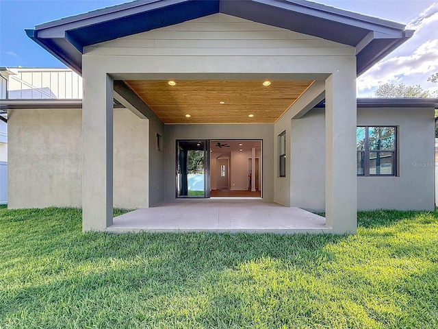 view of exterior entry featuring a patio, stucco siding, and a yard