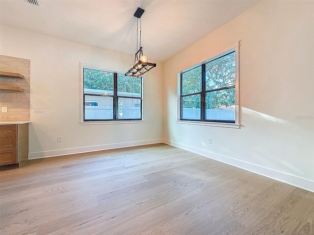 unfurnished dining area featuring light wood-type flooring, baseboards, and visible vents