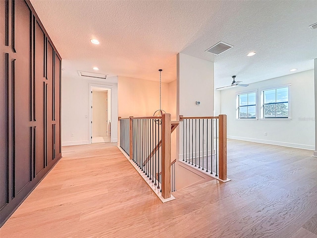 corridor featuring a textured ceiling, an upstairs landing, light wood-style flooring, and visible vents