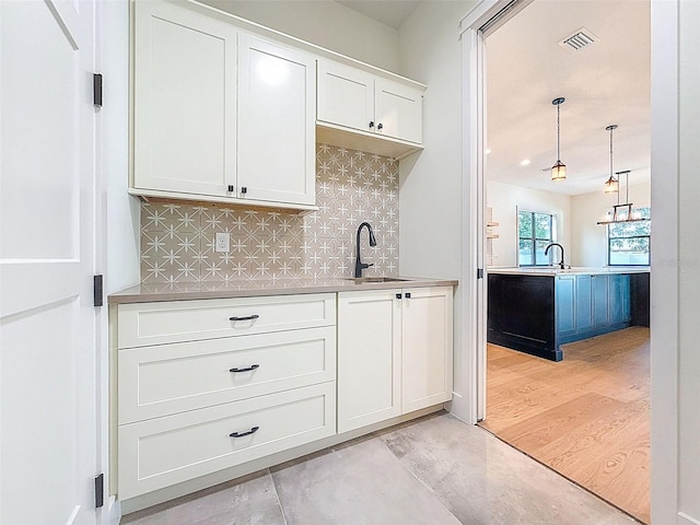kitchen featuring a sink, white cabinetry, tasteful backsplash, visible vents, and pendant lighting
