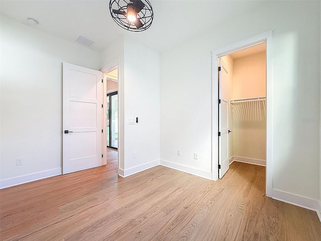 unfurnished bedroom featuring baseboards, a spacious closet, light wood-style flooring, and visible vents