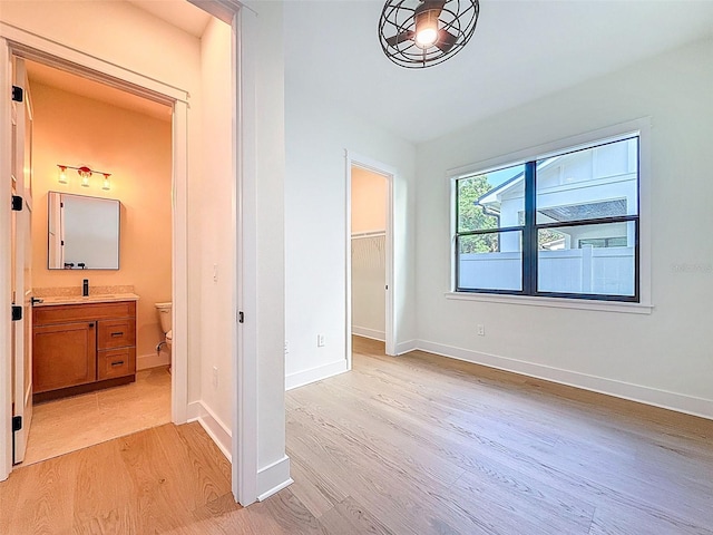 unfurnished bedroom with baseboards, ensuite bathroom, light wood-type flooring, a spacious closet, and a closet