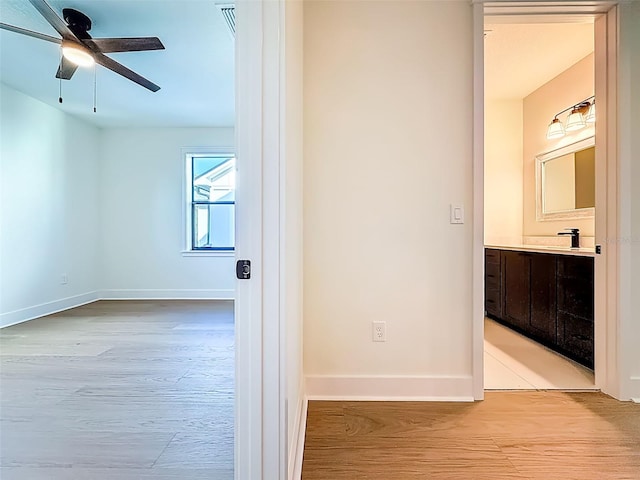 hallway with baseboards, a sink, light wood finished floors, and visible vents