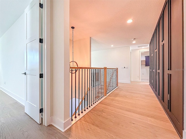 hall featuring a textured ceiling, recessed lighting, baseboards, an upstairs landing, and light wood-type flooring