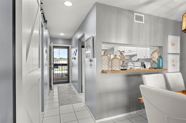 interior space with light tile patterned flooring, a barn door, white cabinetry, under cabinet range hood, and visible vents