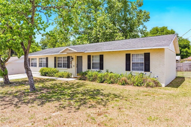 ranch-style home featuring brick siding, a shingled roof, fence, and a front yard