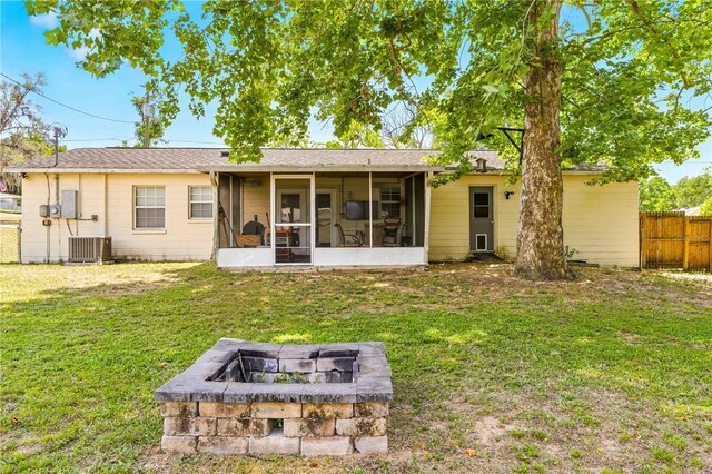 back of property featuring a lawn, a sunroom, fence, cooling unit, and an outdoor fire pit