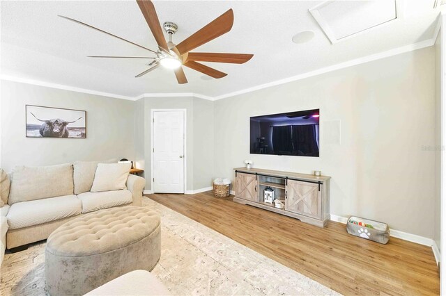 living area with crown molding, wood finished floors, baseboards, attic access, and ceiling fan