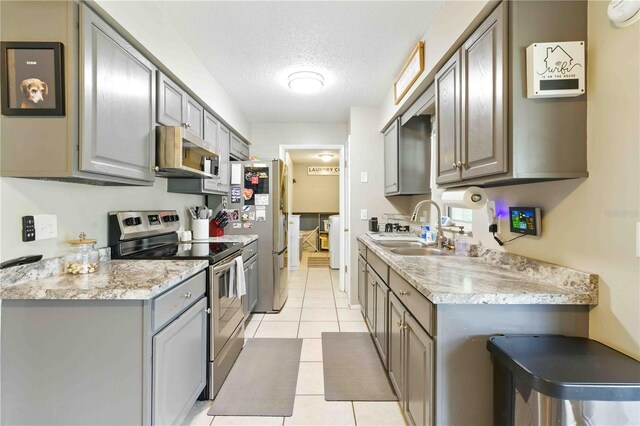 kitchen with light tile patterned flooring, a textured ceiling, a sink, gray cabinetry, and stainless steel appliances