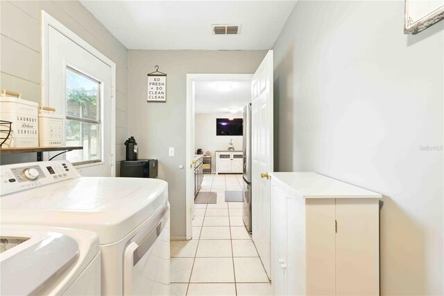 washroom with light tile patterned floors, washing machine and clothes dryer, cabinet space, and visible vents