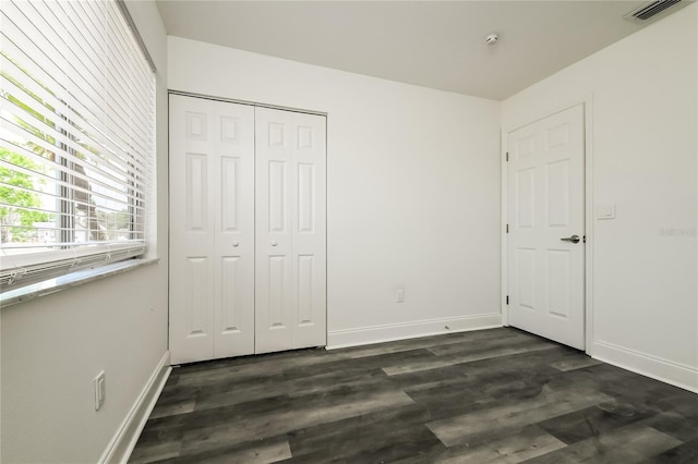 unfurnished bedroom with a closet, baseboards, visible vents, and dark wood finished floors