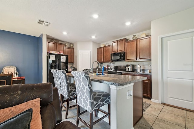 kitchen featuring visible vents, dark countertops, a center island with sink, a kitchen bar, and black appliances