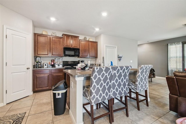 kitchen with black appliances, open floor plan, a breakfast bar, light tile patterned flooring, and an island with sink
