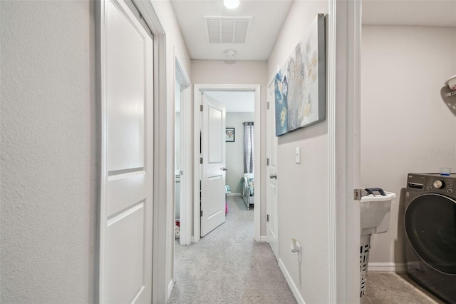 hall with visible vents, washer / dryer, baseboards, and light carpet