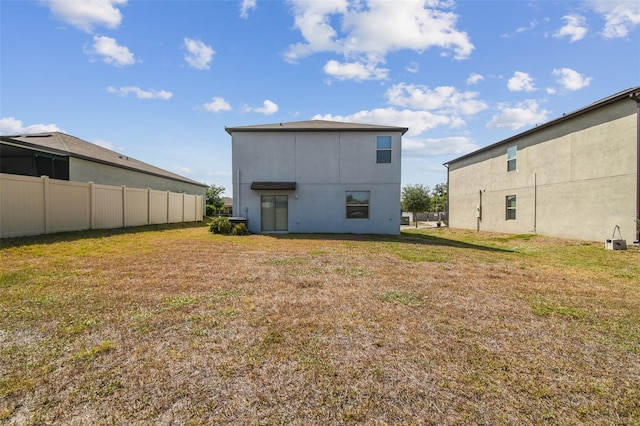 back of house with stucco siding, fence, and a yard