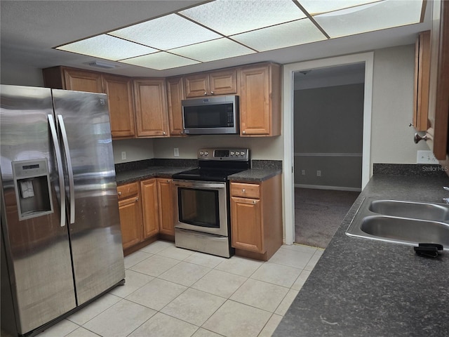 kitchen with brown cabinets, dark countertops, a sink, stainless steel appliances, and light tile patterned floors