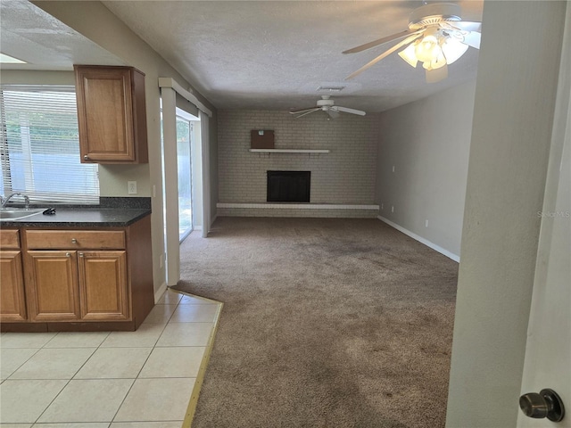 unfurnished living room featuring light carpet, a sink, a brick fireplace, a textured ceiling, and a ceiling fan