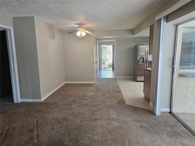 unfurnished room featuring baseboards, a textured ceiling, ceiling fan, and light carpet