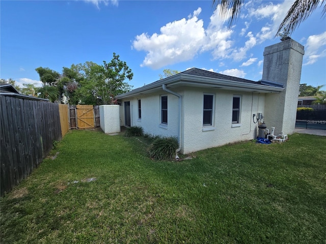 view of side of property with a fenced backyard, stucco siding, a chimney, a gate, and a yard