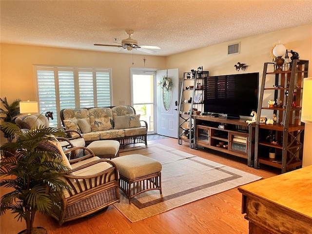 living area with ceiling fan, a textured ceiling, visible vents, and wood finished floors