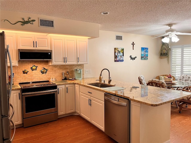 kitchen featuring a sink, a peninsula, stainless steel appliances, a textured ceiling, and light wood-style floors