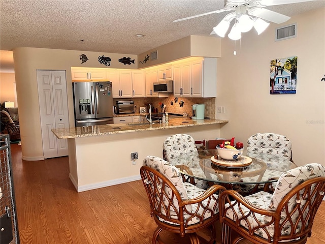 dining space featuring a textured ceiling, visible vents, wood finished floors, and ceiling fan