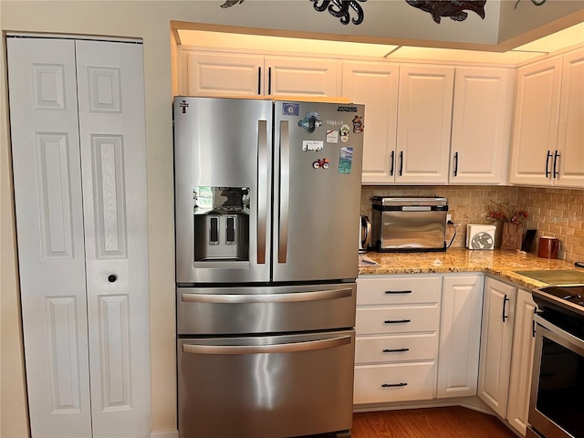 kitchen featuring tasteful backsplash, light stone counters, light wood finished floors, white cabinets, and appliances with stainless steel finishes