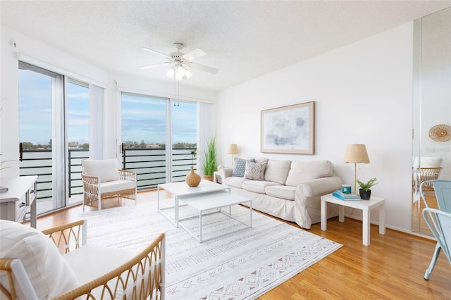 living area featuring wood finished floors, a textured ceiling, ceiling fan, a water view, and baseboards