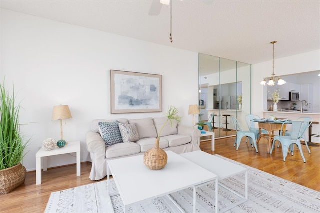 living area with light wood-type flooring and ceiling fan with notable chandelier