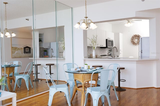 dining space with baseboards, light wood finished floors, and ceiling fan with notable chandelier