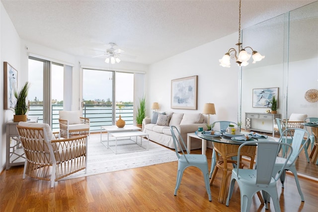 interior space featuring a textured ceiling, a water view, wood finished floors, and ceiling fan with notable chandelier