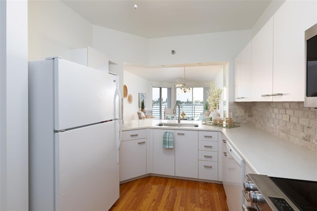 kitchen featuring white appliances, a sink, white cabinetry, backsplash, and light wood-style floors