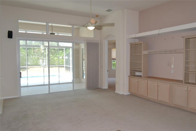 unfurnished living room featuring a ceiling fan, arched walkways, light carpet, and a wealth of natural light