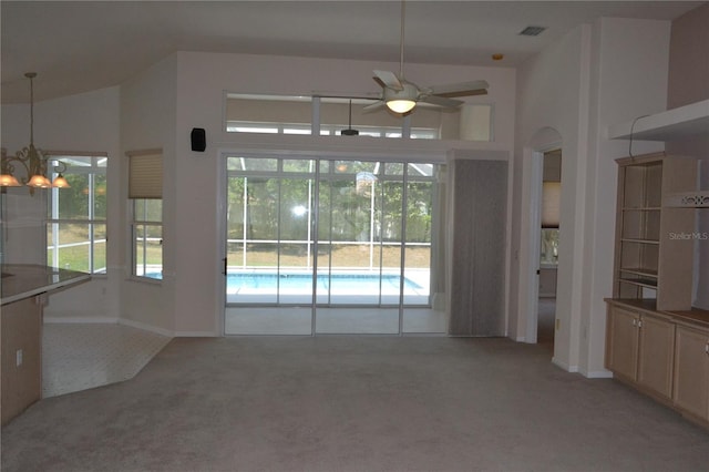 unfurnished dining area with light colored carpet, a wealth of natural light, visible vents, and ceiling fan with notable chandelier