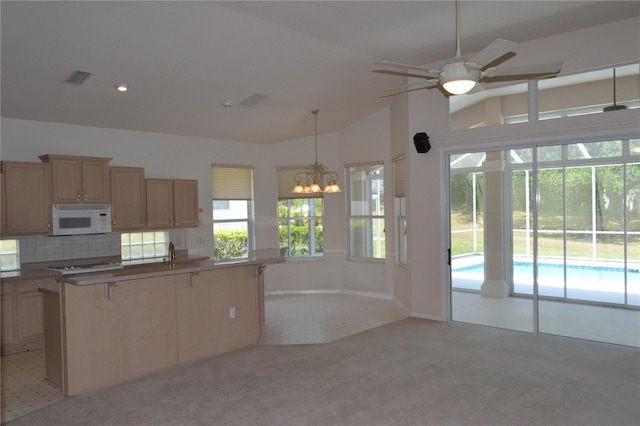 kitchen featuring light colored carpet, a wealth of natural light, white microwave, visible vents, and a center island with sink