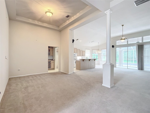 unfurnished living room featuring visible vents, decorative columns, baseboards, light colored carpet, and a tray ceiling