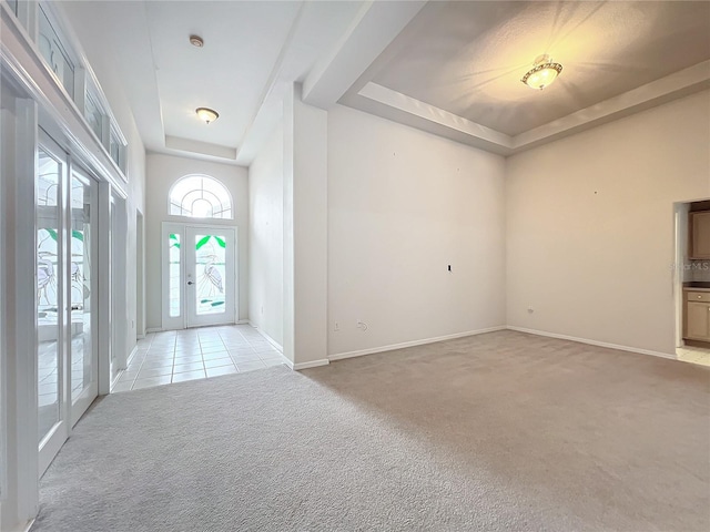 interior space featuring a raised ceiling, baseboards, light carpet, and light tile patterned flooring