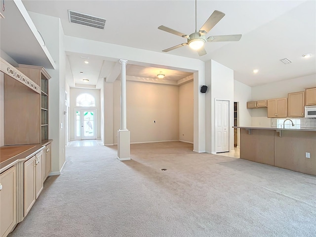 unfurnished living room featuring ceiling fan, light colored carpet, visible vents, a sink, and ornate columns