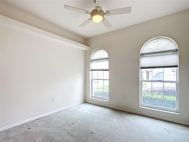 carpeted spare room featuring baseboards and ceiling fan