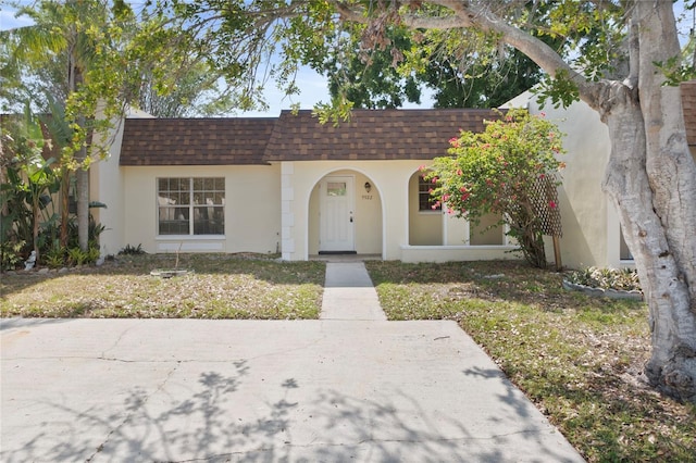 view of front of property with mansard roof, a shingled roof, and stucco siding