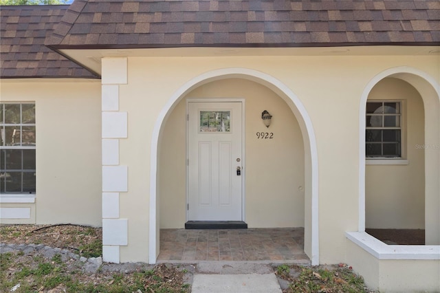 property entrance with mansard roof, a shingled roof, and stucco siding