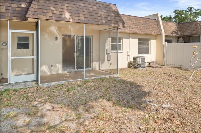 back of house with fence, a shingled roof, stucco siding, central air condition unit, and mansard roof